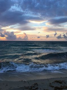 the sun is setting over the ocean with waves crashing on the shore and clouds in the sky