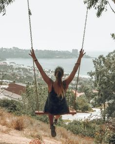 a woman sitting on a swing with her hands in the air