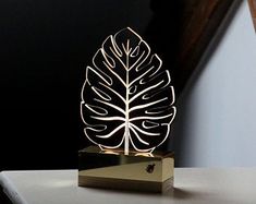 a metal sculpture with a leaf on it sitting on a table next to a lamp