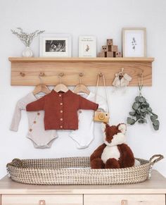 a teddy bear sitting in a basket on top of a wooden shelf next to a baby's clothes rack