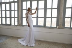 a woman standing in front of a window wearing a white wedding dress with sheer sleeves