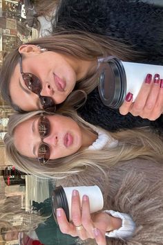 two beautiful young women standing next to each other holding coffee cups and looking at the camera