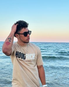 a man standing on top of a beach next to the ocean wearing sunglasses and a t - shirt