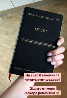 a woman holding up a black book with russian writing on it's front cover