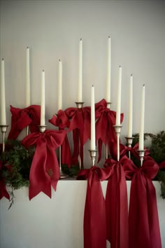 white candles with red bows and greenery in front of them on a shelf against a wall