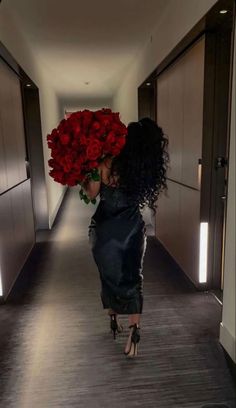 a woman walking down a hallway with red roses in her hand