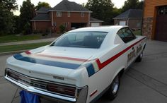 an old white police car parked in front of a house with red, white and blue stripes on the hood