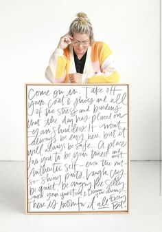 a woman leaning against a sign with writing on it and holding her head in her hands