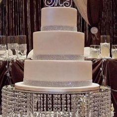 a three tiered white wedding cake with crystal decorations on the top and bottom layer