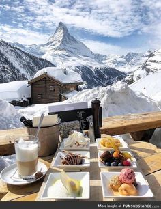 a table topped with plates of food on top of a snow covered slope next to a mountain