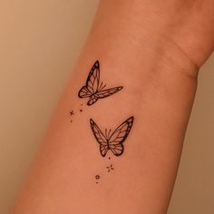 two butterfly tattoos on the wrist and arm, one is black with white butterflies flying around it