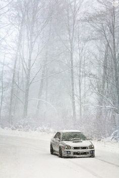 a car driving down a snow covered road in the middle of winter with trees behind it