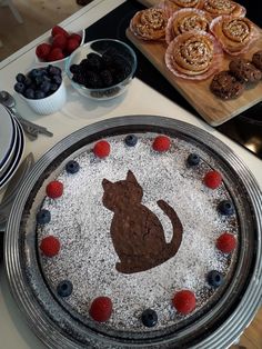 there is a cake with a cat on it and berries in the bowl next to it