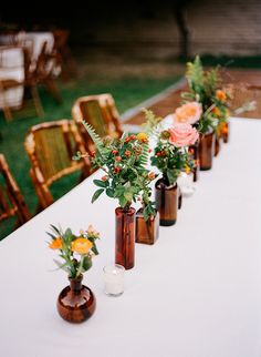 several vases with flowers are lined up on a long table in front of chairs