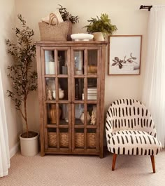 a living room with a chair, potted plant and glass fronted cabinet in the corner