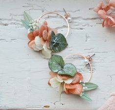 a pair of hoop earrings with flowers and leaves hanging from them on a white wooden surface