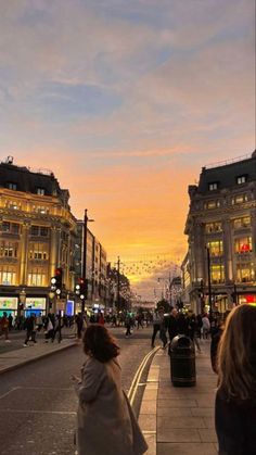 people walking down the street at sunset in an area with tall buildings and traffic lights