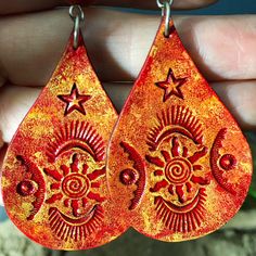 Crimson suns with spiral centers, stars, and moon shapes add celestial magic to these bright, handcrafted leather earrings, with carnelian accent beads. Generously sized but light as a feather.  Lightweight and comfortable, I cut these from vegetable tanned leather, and stamped designs into their surface. Then I dyed them red, and surface textured them with golden yellow and warm orange tones, to accent the tooled design. I sealed them for water resistance, suspended them under carnelian beads, and finally, fastened them to a pair of hypoallergenic french hooks: surgical steel.  One of my photos shows the earrings next to a standard US quarter, for size reference.    P.S. My model is a mannequin, so these earrings have never been in human ears. You will receive the exact earrings that I ph Spiritual Sun Design Jewelry For Festival, Orange Teardrop Jewelry For Festivals, Bohemian Star-shaped Jewelry For Festivals, Bohemian Star Jewelry For Festivals, Bohemian Star-shaped Festival Jewelry, Unique Sun And Moon Design Dangle Jewelry, Handmade Red Star Jewelry, Red Teardrop Jewelry For Festival, Spiritual Sun And Moon Design Earrings For Festival