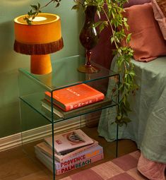 a glass table with books on it and a lamp next to it in front of a green wall