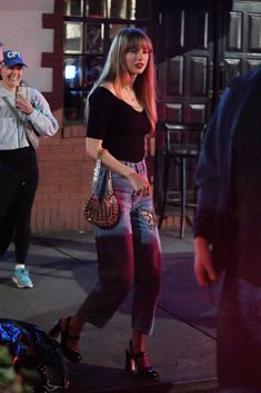 a woman in black shirt and jeans walking down street with handbag on her hip