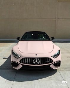 the front end of a pink mercedes benz coupe parked in a parking lot next to a building