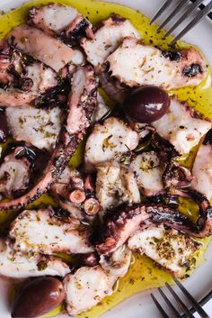 an octopus dish with olives and herbs on a white plate next to a fork