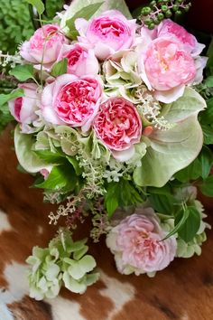 a bouquet of pink flowers sitting on top of a cow print table cloth with greenery