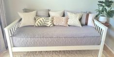 a white daybed with lots of pillows on it in front of a window and potted plant