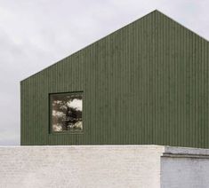 a green building with a window on the side and a brick wall in front of it