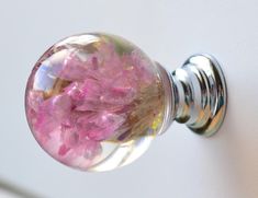 a glass door knob with pink flowers in the center on a white wall behind it