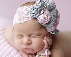 a newborn baby wearing a pink headband and holding her hand up to her ear