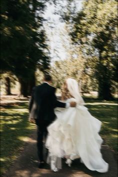 a bride and groom walking down a path in the park holding each other's hands