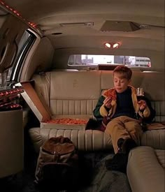 a young boy sitting in the back of a car eating pizza