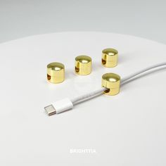 three gold - plated plugs are connected to a white cord on a white surface