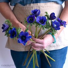 a woman holding a bunch of blue flowers in her hands with the stems still attached