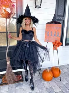 a woman dressed as a witch holding a broom and standing in front of a door