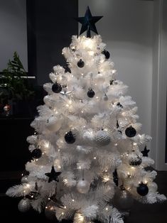 a white christmas tree decorated with black and silver baubles, stars and ornaments