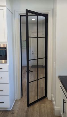 an open door leading into a kitchen with white cabinets and black counter tops on both sides