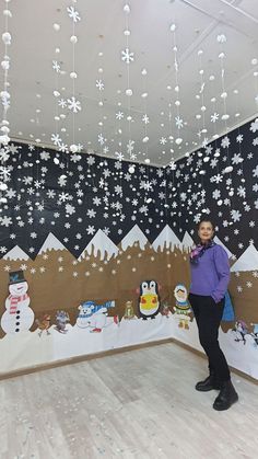 a woman standing in front of a snow scene with penguins and snowflakes hanging from the ceiling