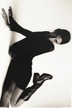 a black and white photo of a woman leaning against a wall with her hands in the air