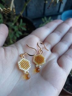 a hand holding two small beaded earrings in it's palm, next to a potted plant