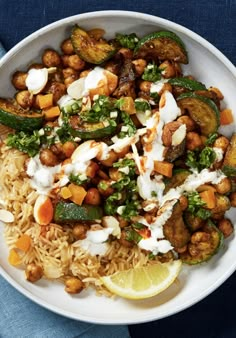 a white plate topped with rice and veggies next to a lemon wedge on a blue cloth