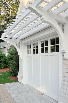 a white garage with an attached pergolan over the door and side walk way