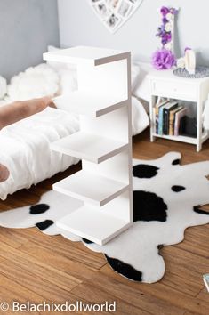 a person is holding up a book shelf in the middle of a room with cow rugs on the floor