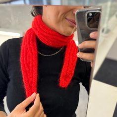 a woman wearing a red scarf and holding a cell phone in her hand while standing next to a counter