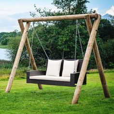 a wooden swing set with black cushions in the grass next to a body of water