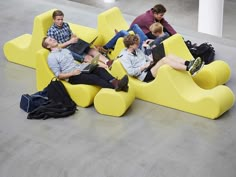 four people sitting on yellow couches with laptops and backpacks in the middle