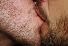 a close up of a man with his mouth open to kiss the nose of another man