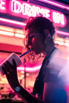 a woman drinking from a straw in front of a neon sign