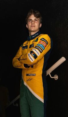 a man standing in front of a black wall wearing a yellow and green racing suit